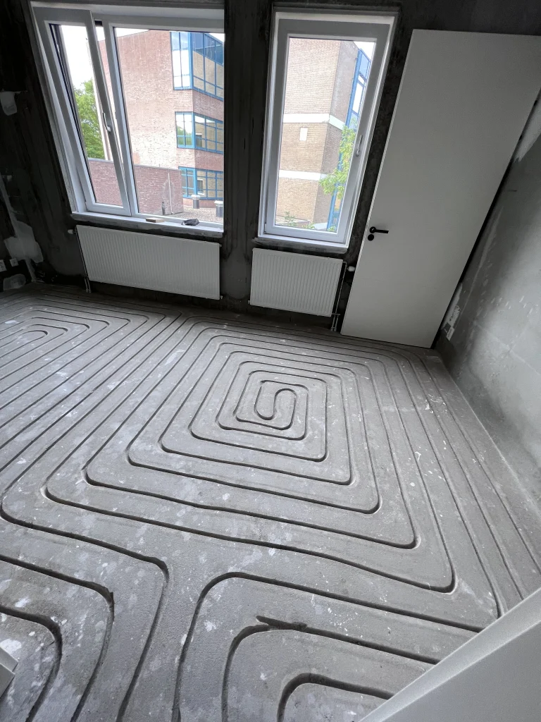 Kamer met twee ramen waarin vloerverwarming in een slakkenhuispatroon is ingefreesd